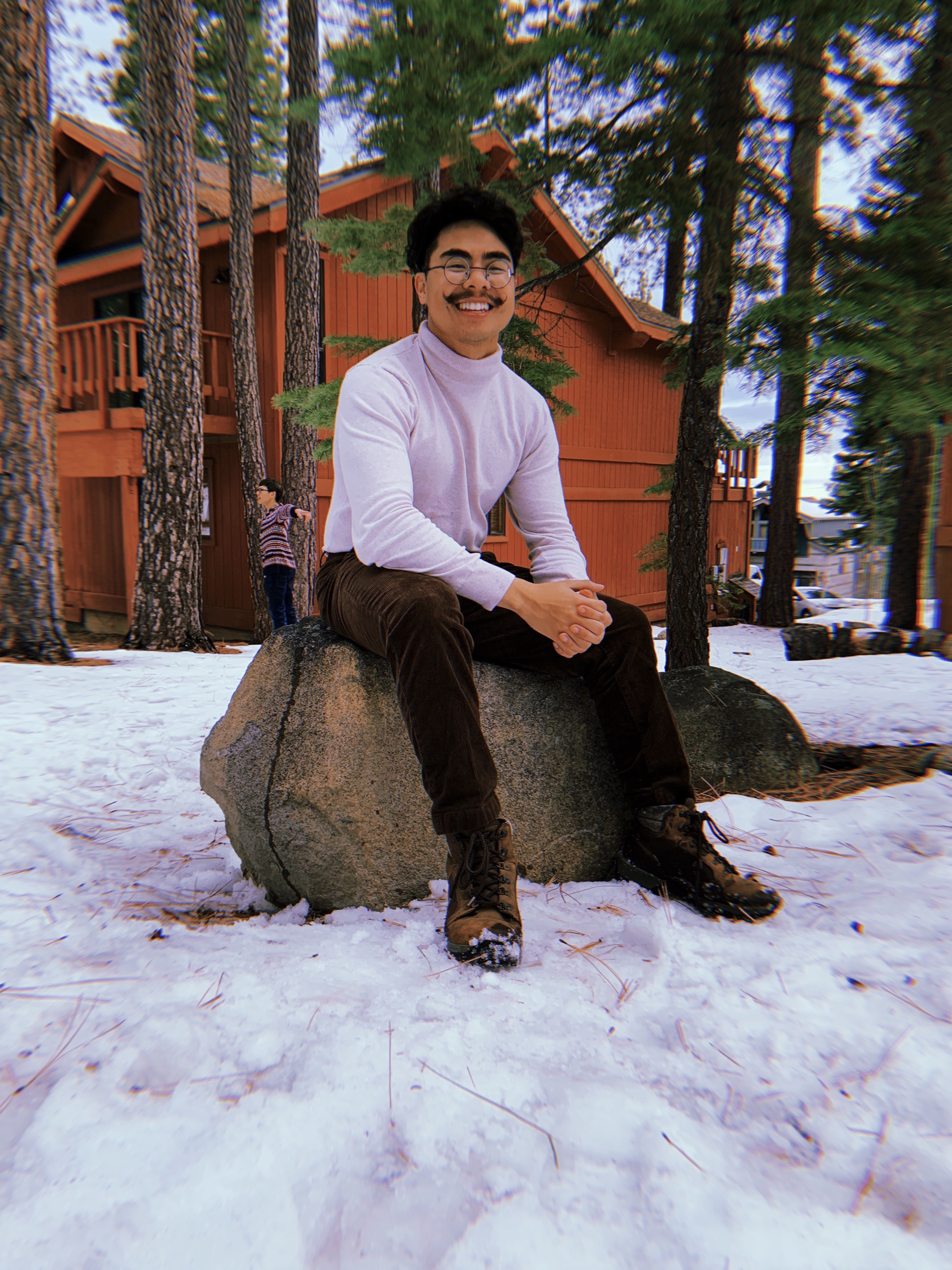 vietnamese man with moustache sitting on a log in the snow.